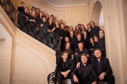 Kammerchor der HfMT viele schwarz gekleidete Menschen lachend auf geschwungener Innentreppe
