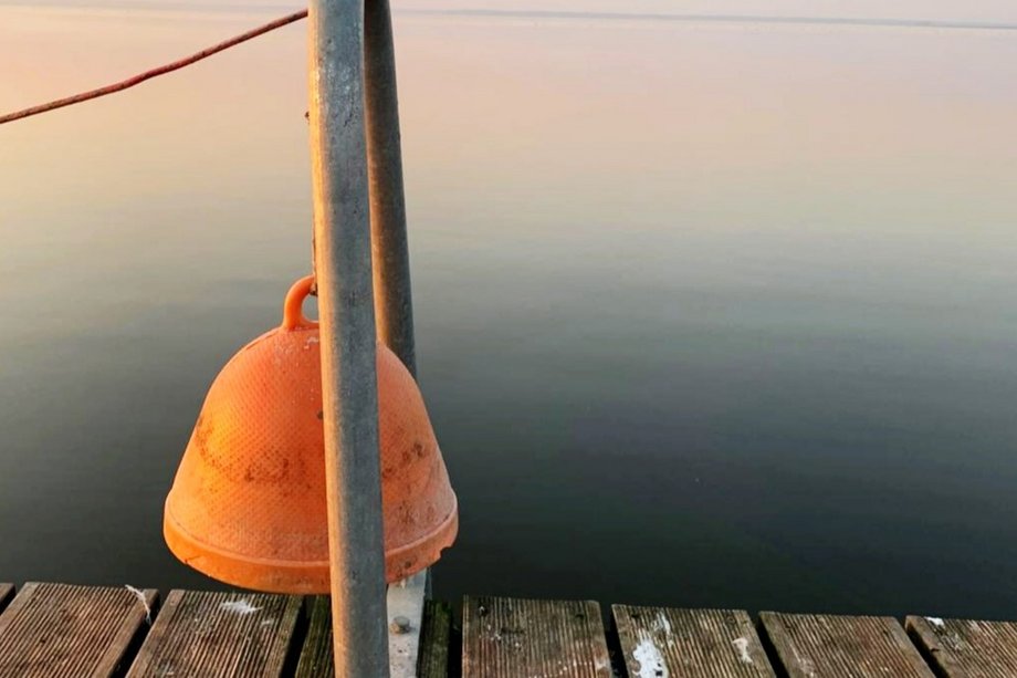 Die Kunst des Hörens orange-farbene Glocke am Steg vor einem ruhigen See