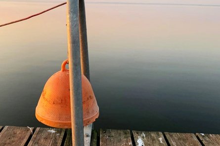 orange-farbene Glocke am Steg vor einem ruhigen See