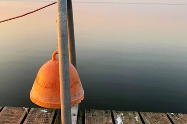 orange-farbene Glocke am Steg vor einem ruhigen See