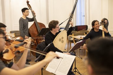 six people with baroque stringed instruments and music stands