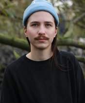 Portraitfoto von Till Dogan Ertener vor einem Ast.