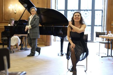 2026-04-14 Frauenliebe und Leben Frau auf einem Stuhl schaut in die Kamera, im Hintergrund ein Flügel