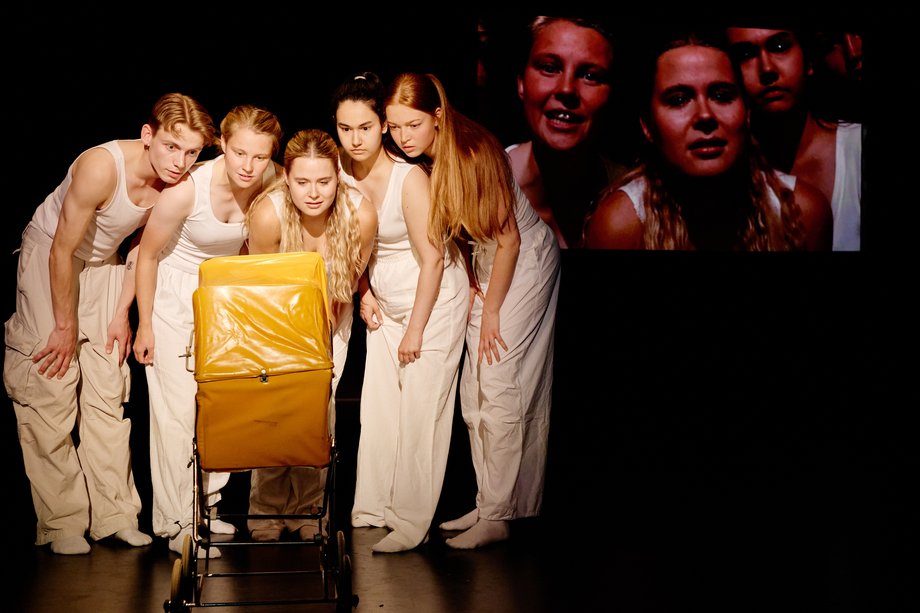 A group stands around a yellow baby carriage and looks inside.