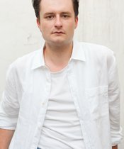 Portrait photo of Aaron Brömmelhaup Brown-haired person with a white shirt.