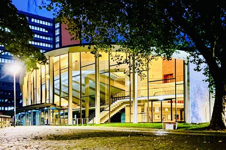 Audimax Ansicht eines Gebäudes mit Glasfassade am Abend im Schein einer Straßenlaterne