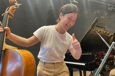 Musician with cello in front of a grand piano, thumbs up and laughing