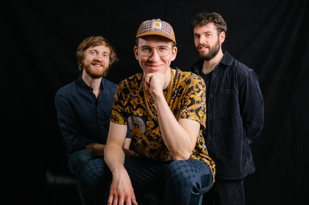 Gruppenfoto von drei Männern mit dunklem Hintergrund