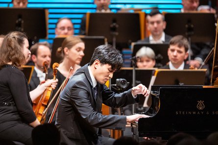 Person spielt Flügel, Orchester im Hintergrund