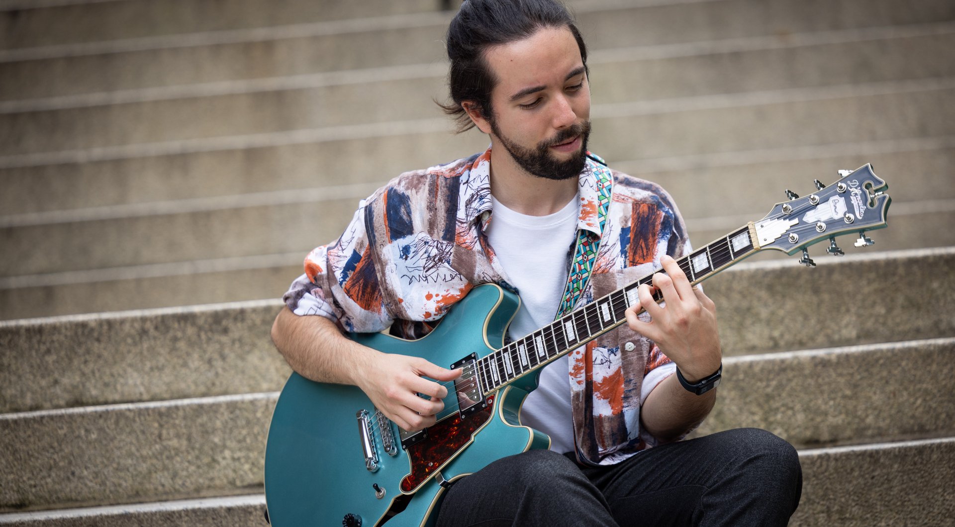 Man sits on a gray stone staircase with an electric guitar and plays