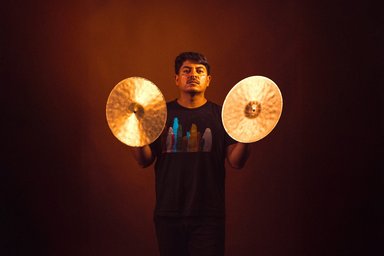 2025-12-14RicardoChichoCastillo Mann mit zwei Becken in den Händen, frontal mit braunem Hintergrund