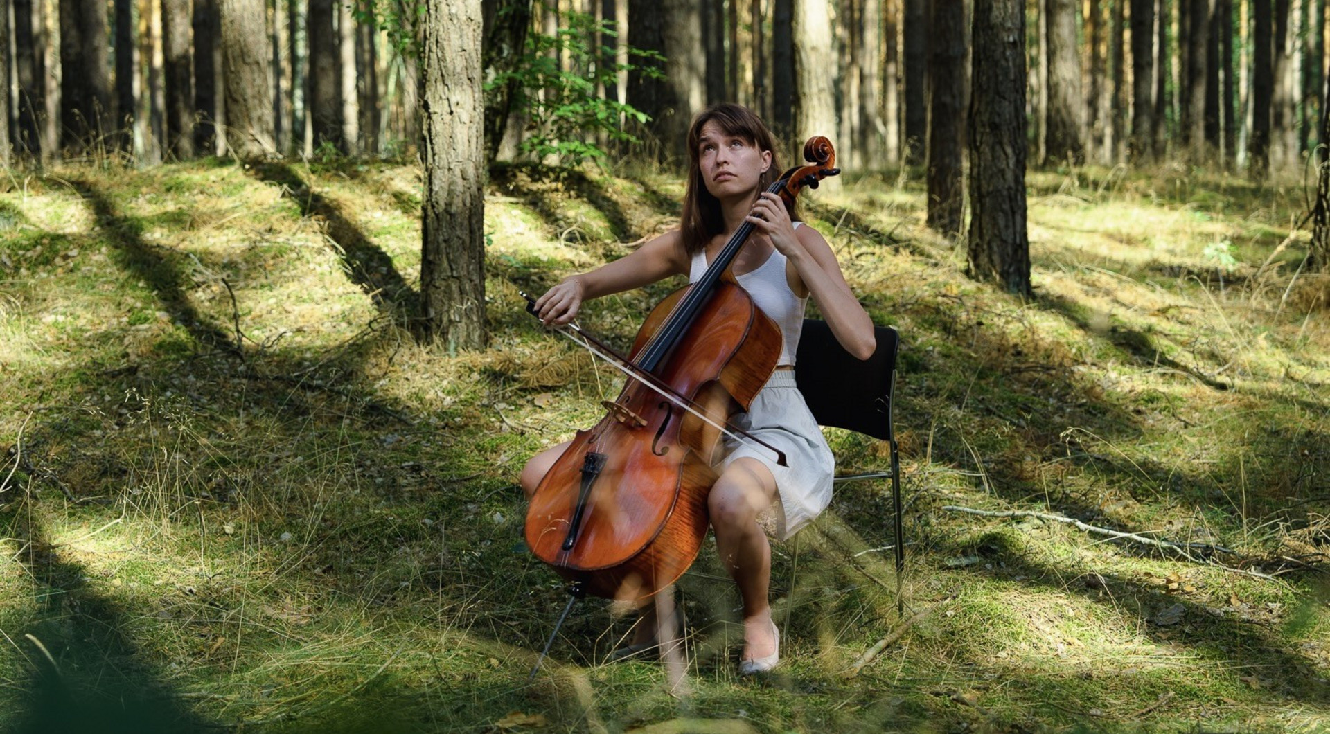 Cellistin sitzt mit ihrem Instrument im Wald