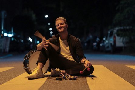 ein Mann, nachts auf einem Zebrastreifen sitzend, mit Percussioninstrumenten