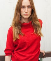 Rothaarige Person mit rotem Pullover.