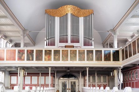 Blick in hellen Kirchenraum mit Sitzreihen und Orgel auf Empore