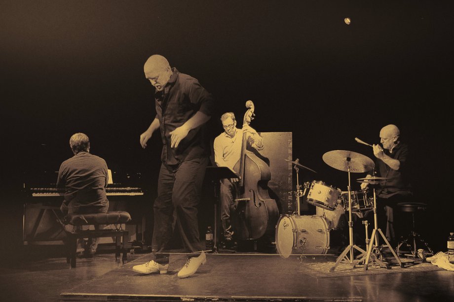 2026-04-02 steppender Mann auf der Bühne mit Trio aus Klavier, Kontrabass und Schlagzeug