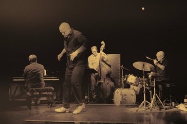 tap-dancing man on stage with trio of piano, double bass and drums