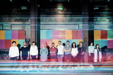 11 people standing next to each other facing the camera; distorted colors