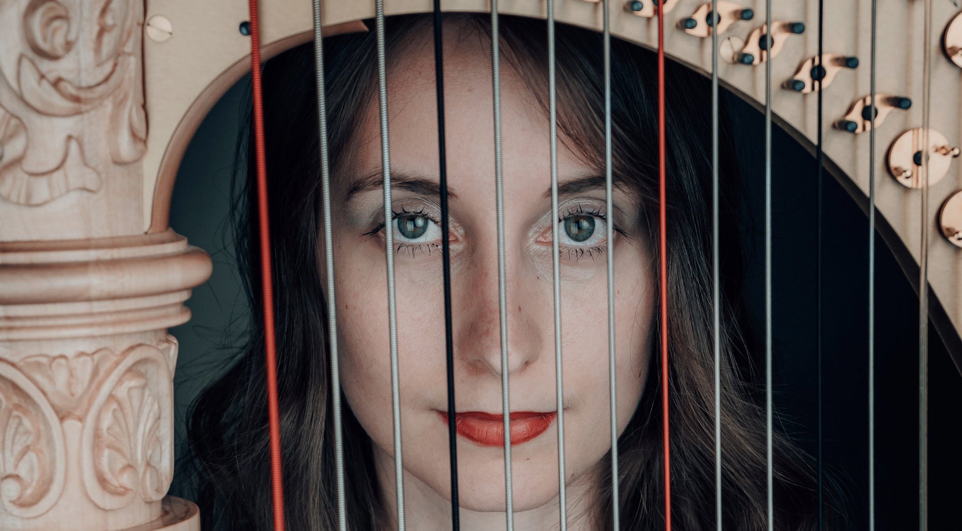 Chiara Sax looks into the camera through the strings of her harp