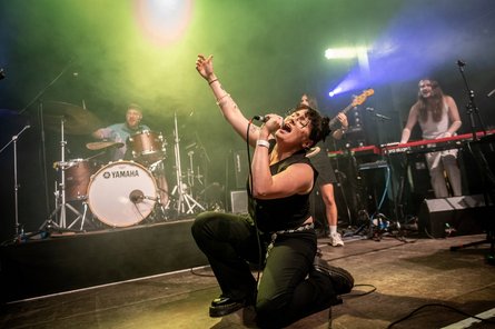 Foto von einer Frau mit Band, die auf einer Bühne singt.
