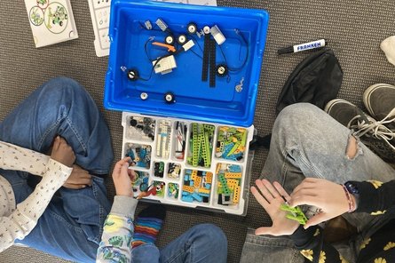 Code week 2025 Kiste mit Legosteinen und Kabeln. Reingreifende Kinderhände, von oben