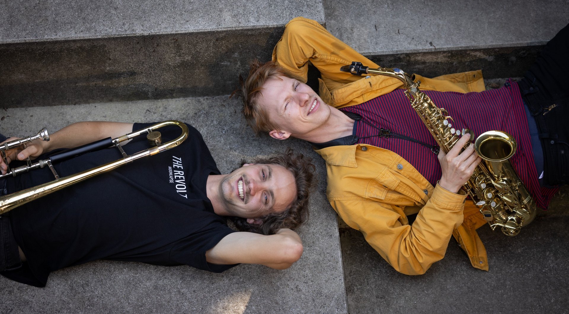 Posaunist und Saxophonist mit Instrument auf Boden liegend von oben fotografiert