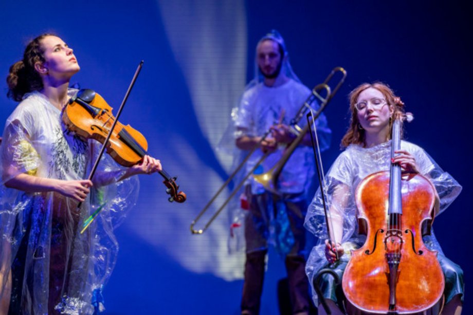 Stegreif Orchester: freemahler – what the earth tells us drei Personen mit Instrumenten, die Regenpochos tragen