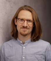 Portrait.JanisBrucker Portrait eine Mannes mit Brille und halblangen Haaren, hellblaues Hemd