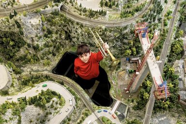 Kind mit einer Trompete steht in einer Miniaturlandschaft; Ansicht von oben