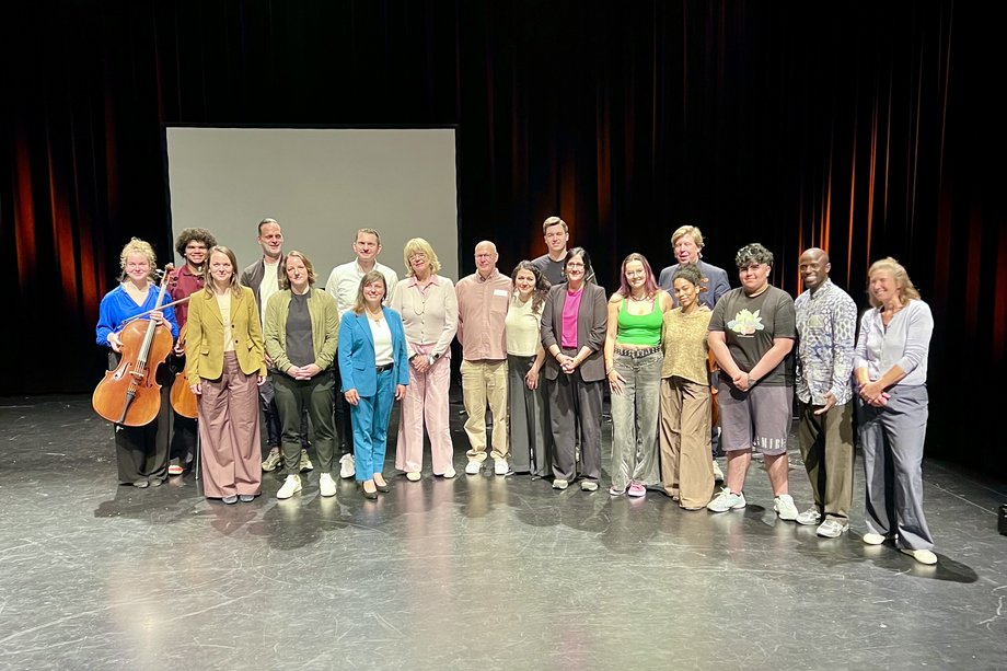 Viele Menschen stehen für ein Gruppenfoto auf einer Theaterbühne
