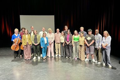 Viele Menschen stehen für ein Gruppenfoto auf einer Theaterbühne