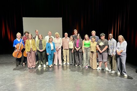 Viele Menschen stehen für ein Gruppenfoto auf einer Theaterbühne