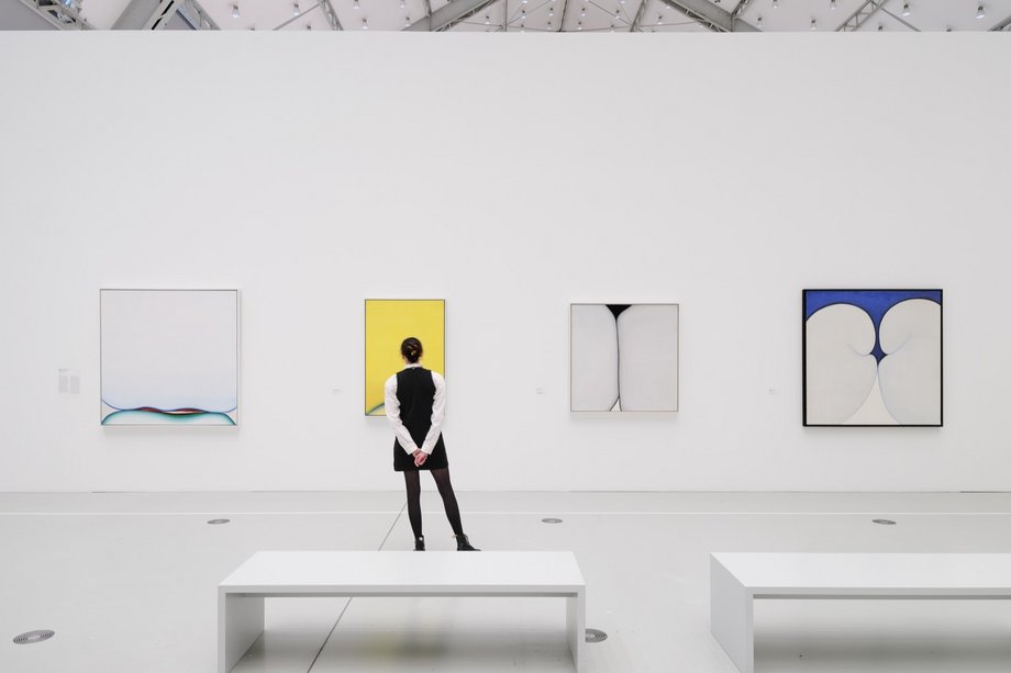 Huguette Caland 3 zu 2 Frau von hinten in einem großen Ausstellungshalle vor 3 Bildern