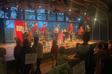 Kinderkonzert Live Music Now Musicians and children on the stage of the JazzHall presenting the flowers