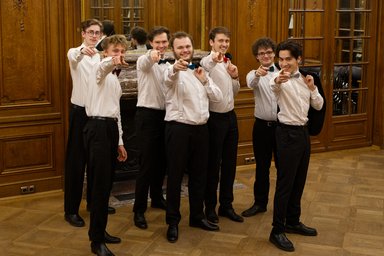 the male choir stands facing the camera and points to it