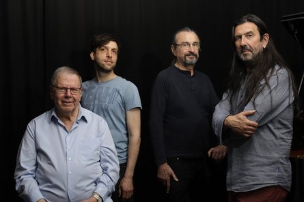 Gruppenfoto von vier Männern vor einem schwarzem Hintergrund