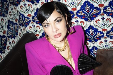 Lady Bitch Ray in a pink suit with horns in front of detailed painted tiles