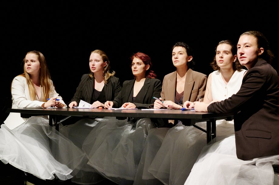 Actresses sit around a table and look into the audience